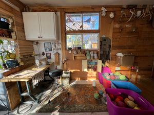 A view of a fiber artists studio with a rainbow of yarn in totes, a sewing machine, Persian rugs on the floor