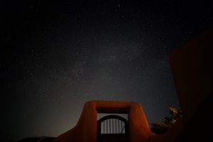 A photo of the night sky filled with stars. In the center foreground is an adobe gate illuminated from the right. 