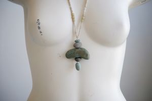 A white colored female formed mannequin wears a necklace of smooth green stones and white glass beads
