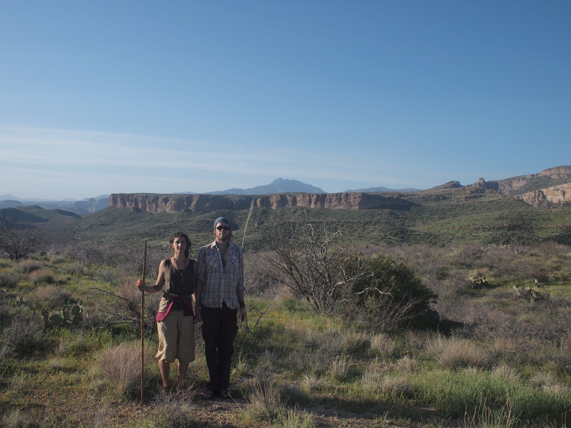 A man and woman standing hand in hand in a desert mountain landscape. 