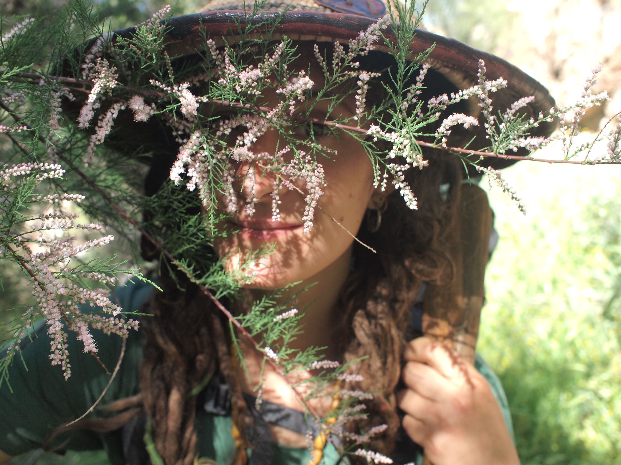 Woman peeking gout from behind a green branch blowing with small light pink flowers