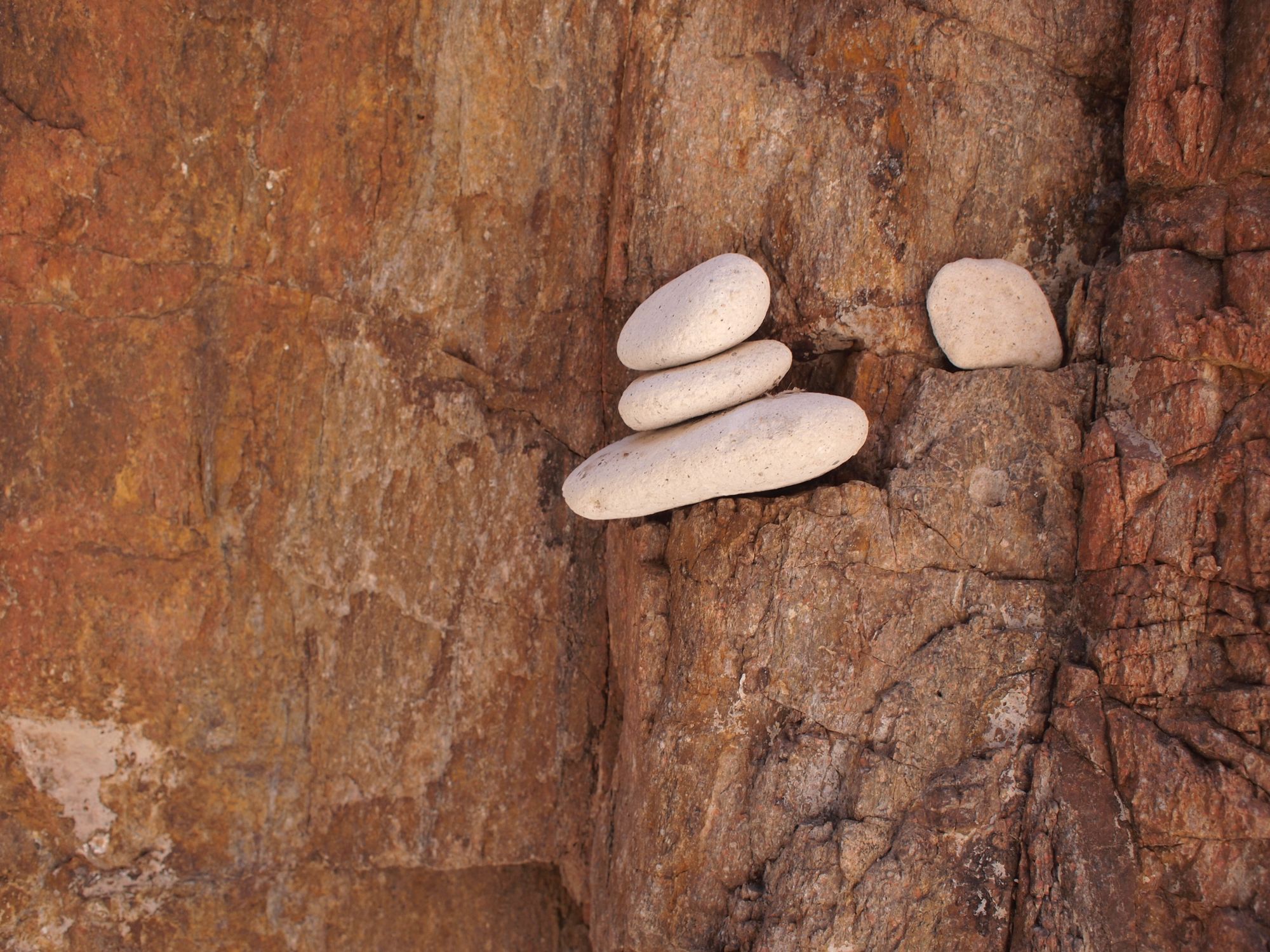 Three round, white stones stacked on top of each other, sitting on a red-orange canyon wall. 