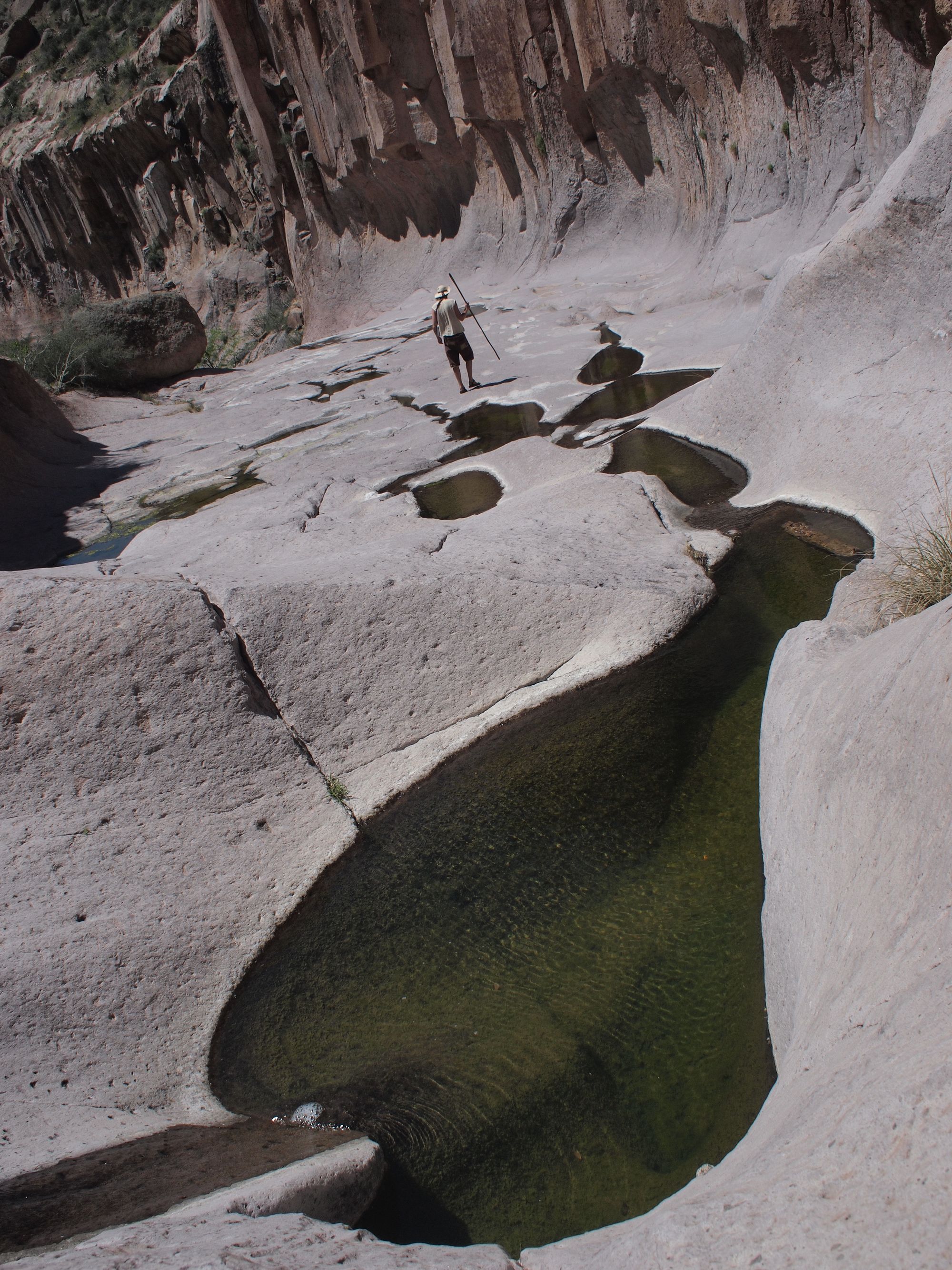 Man walking through a narrow basalt canyon with small water filled pools running through.