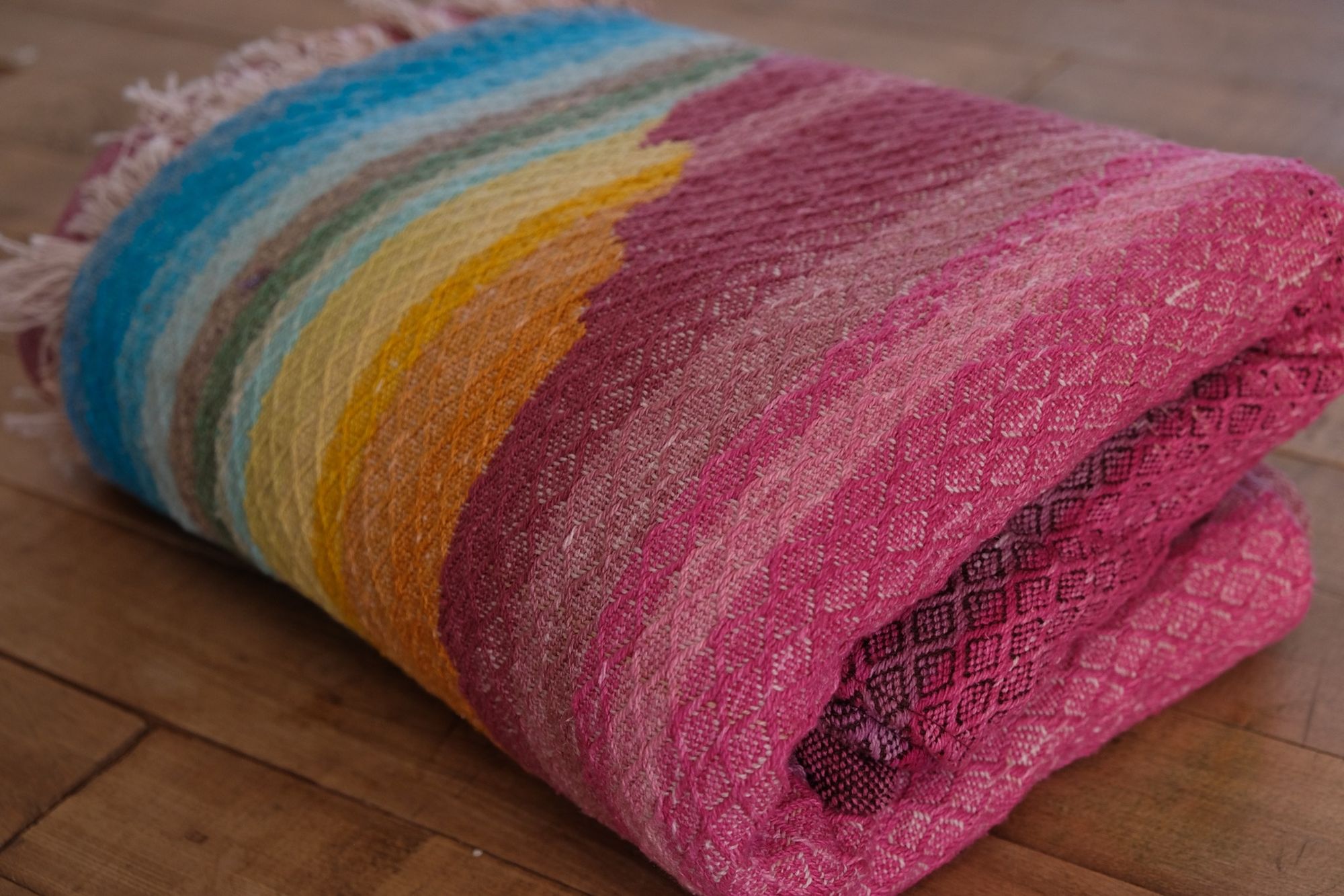 Brightly colored fabric in pink, yellow, orange, blue, cream, green and purple is folded on a wooden floor