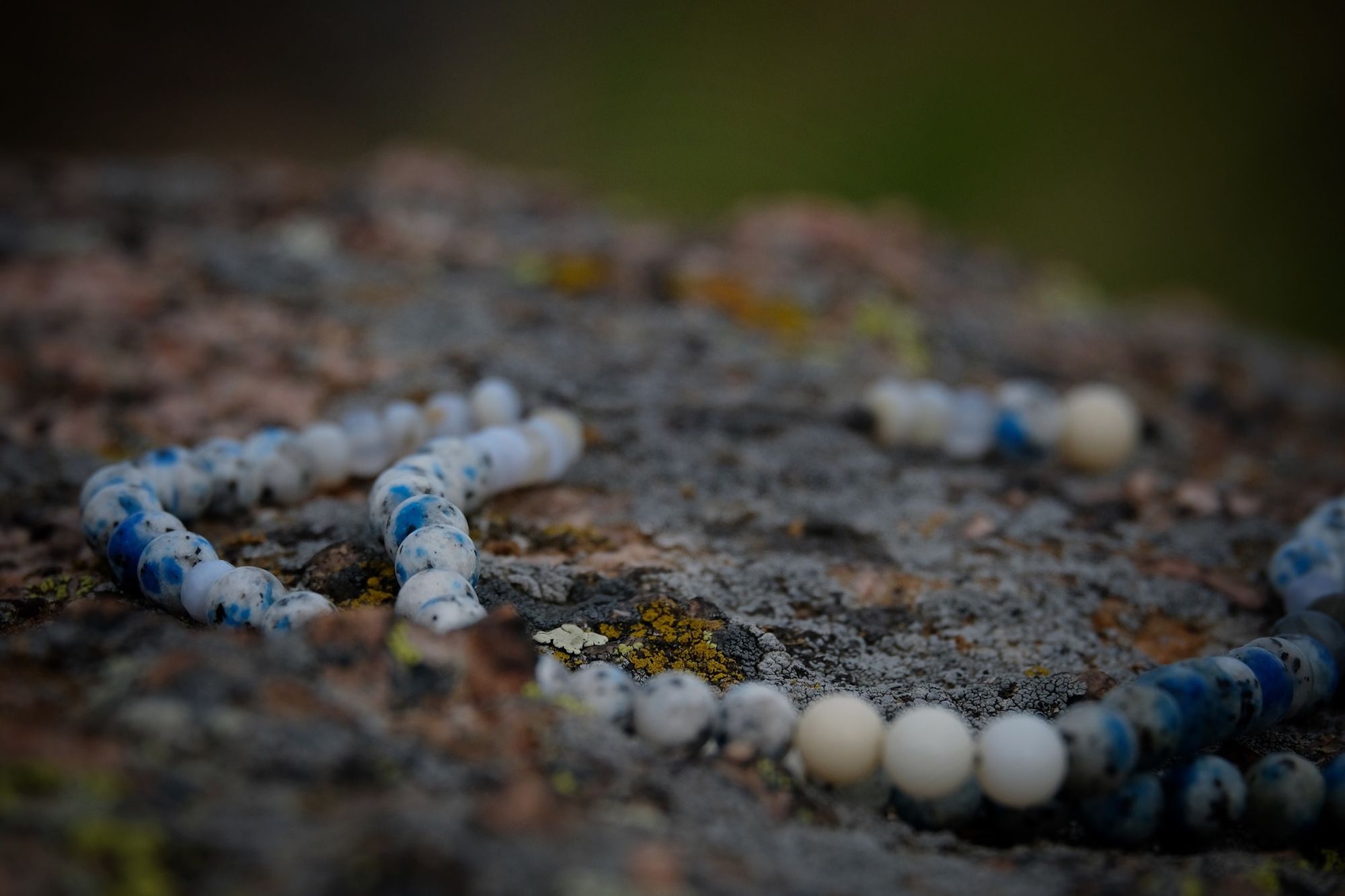 A necklace of crystal and semi precious stones lays on a lichen covered boulder in the mountains