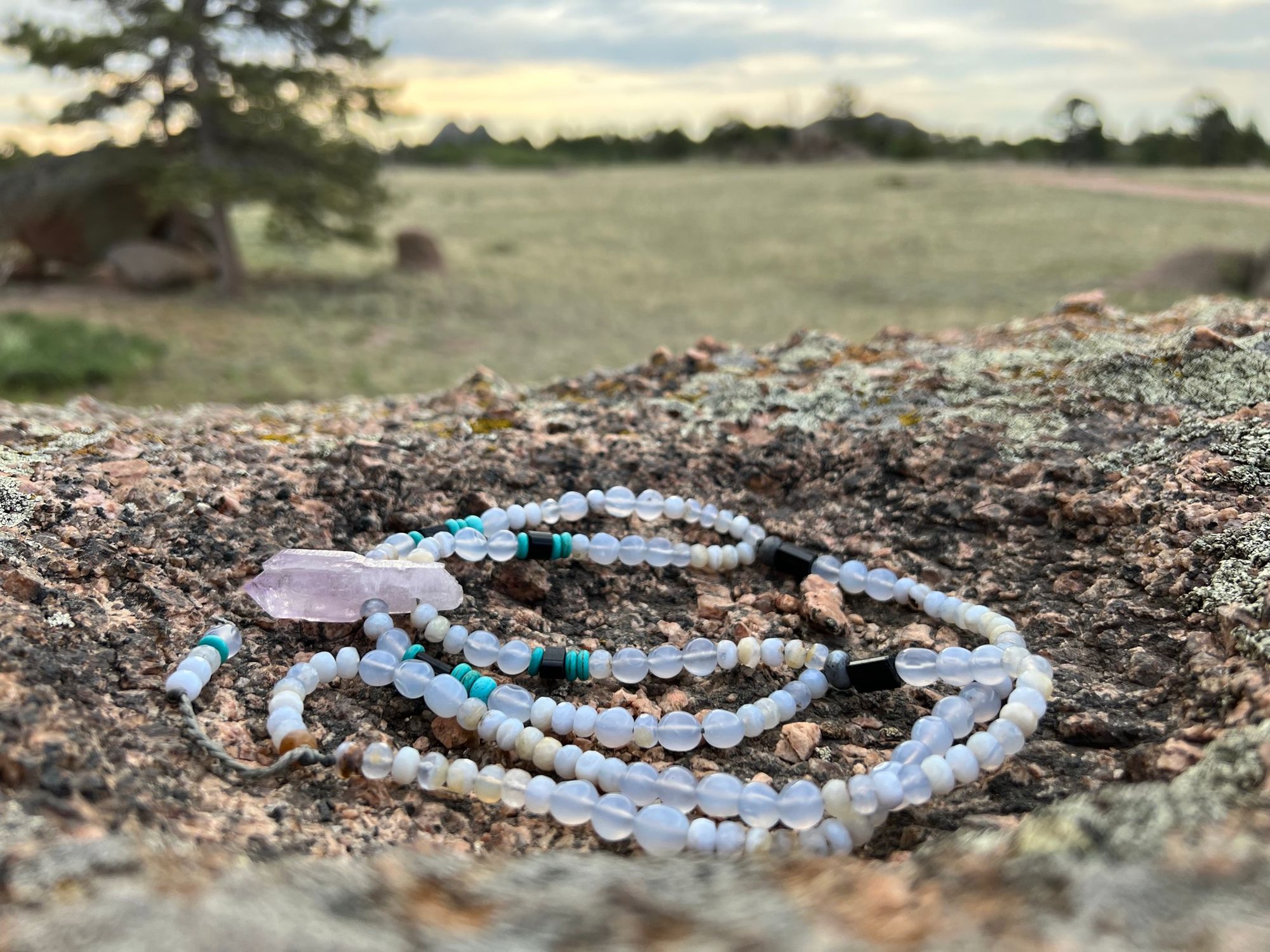 A necklace of crystal and semi precious stones lays on a lichen covered boulder in the mountains