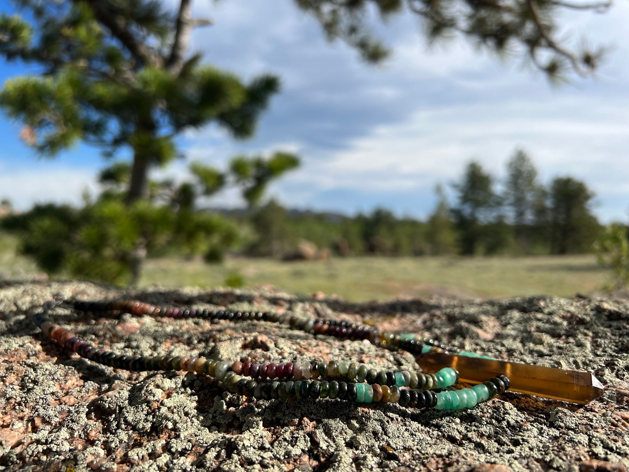 A necklace of crystal and semi precious stones lays on a lichen covered boulder in the mountains