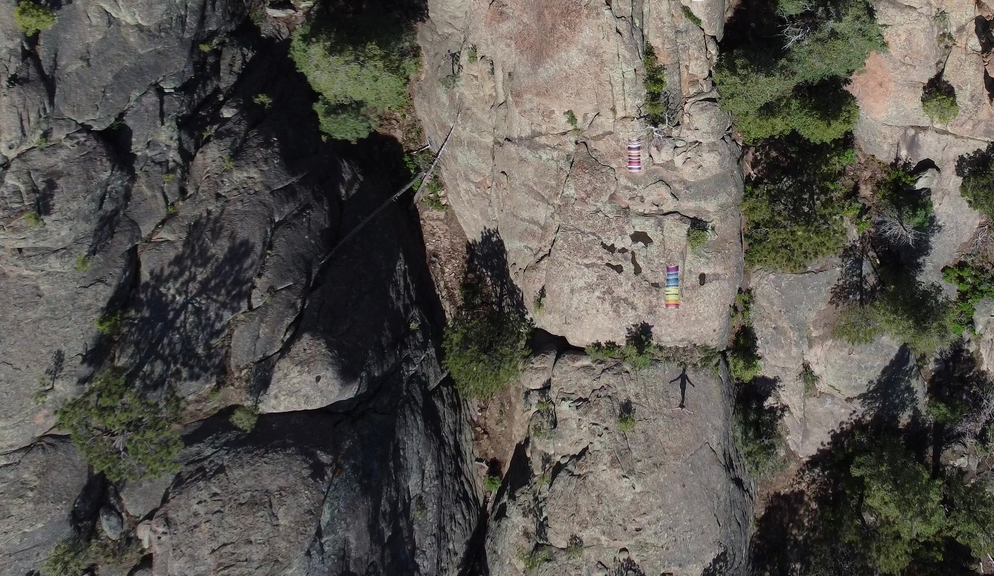 Two blankets, one rainbow stripe one maroon, tan and blue, lay on giant monolithic rocks in the forest