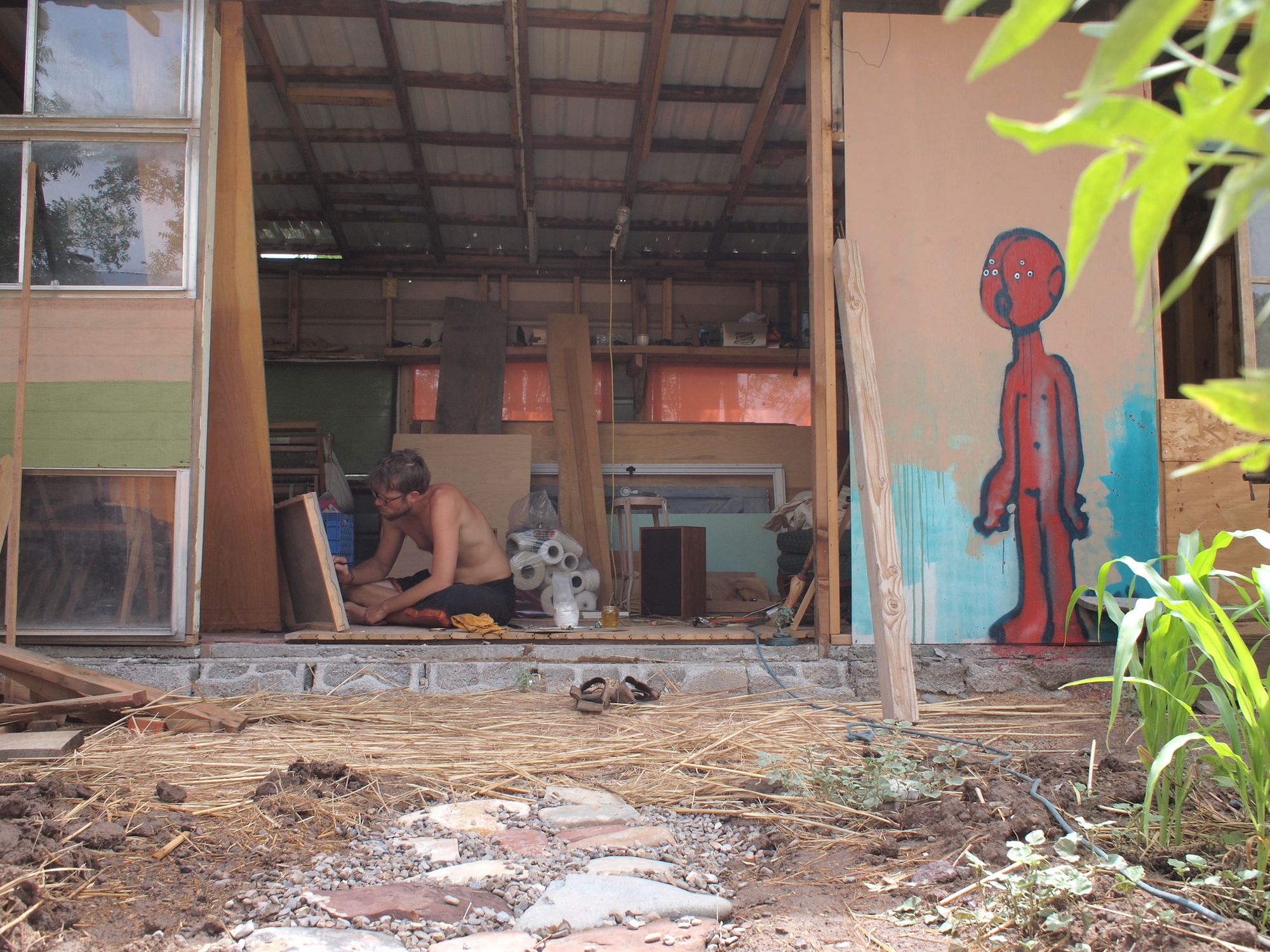 A man sits on the ground painting in the doorway of an unfinished building.