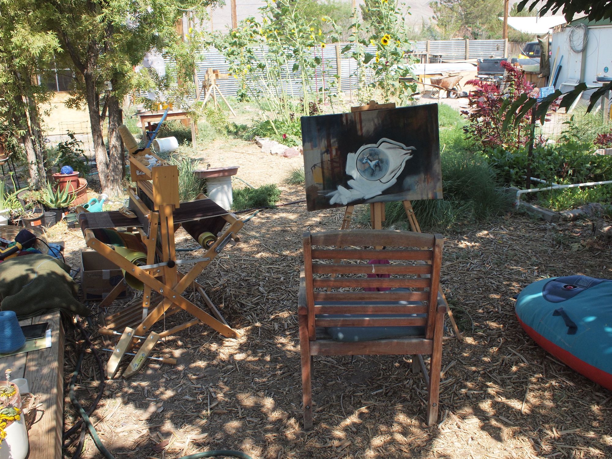 A overgrown backyard with a loom and canvas on easel setup as a workspace for artists.