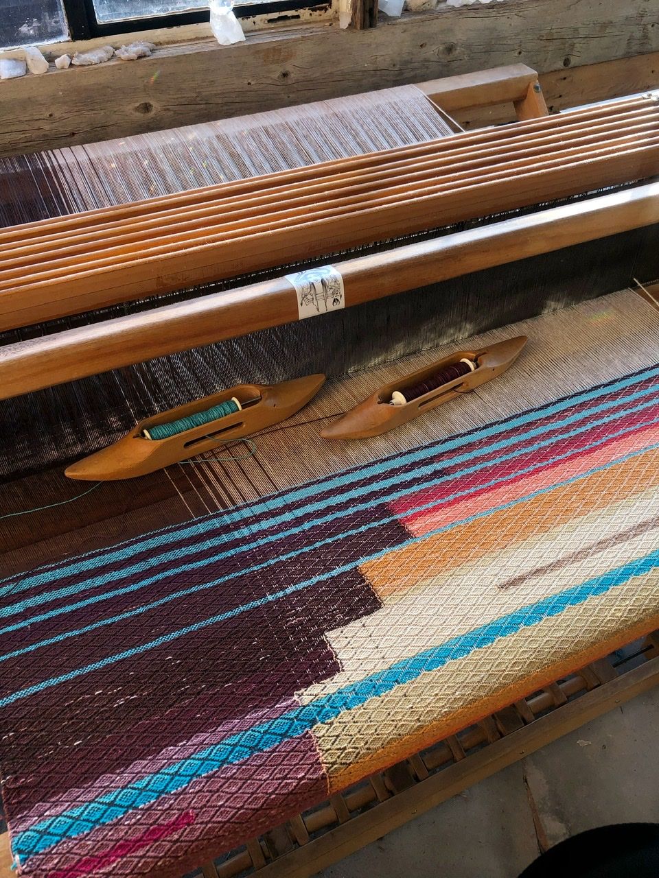 A view from above of a loom with a large graphic shaped, multi colored weaving on it in purples, yellows, blue, pink and red