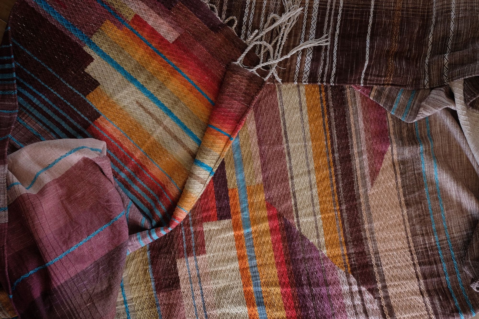 Handwoven fabric with a diamond texture pattern in natural browns, grey, purples, reds, turquoise, yellow, orange and pink.