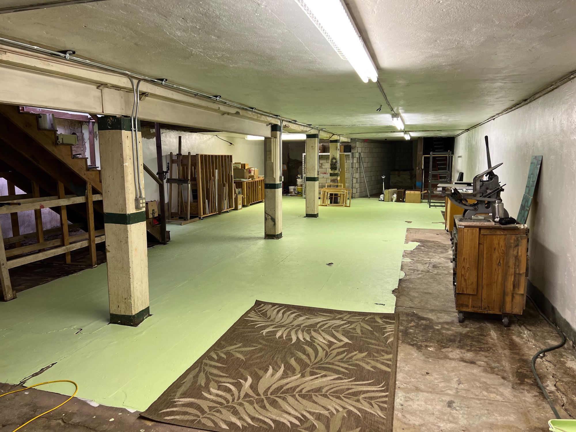 A large basement with many things neatly organized, including a letter press and racks of paintings.