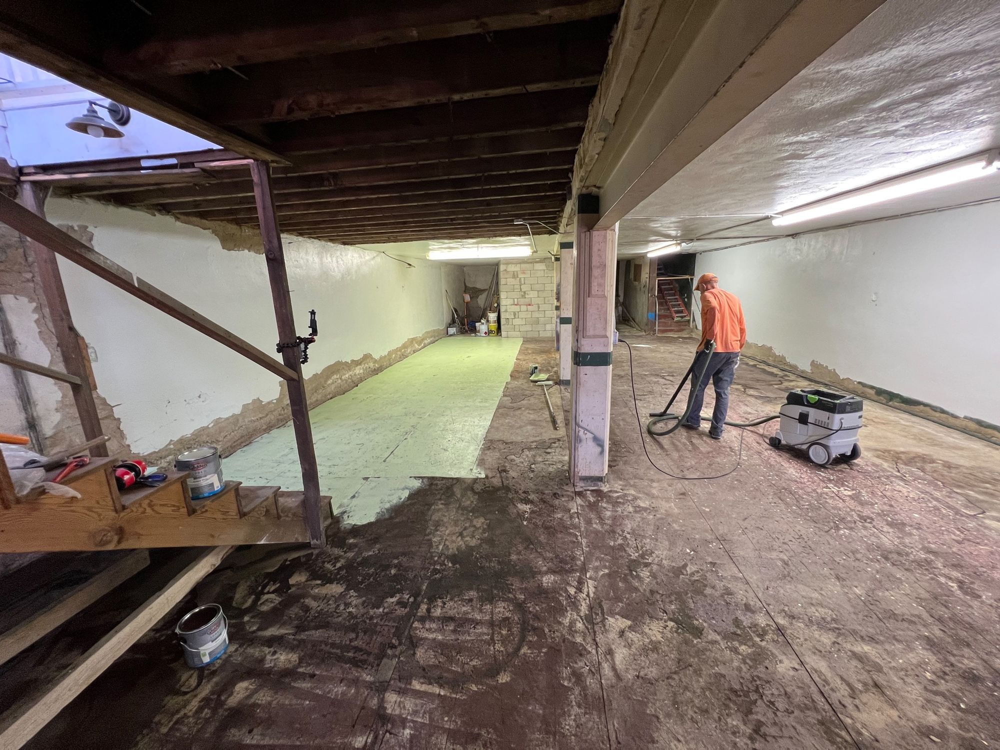 A man in an empty basement vacuuming the floor. 