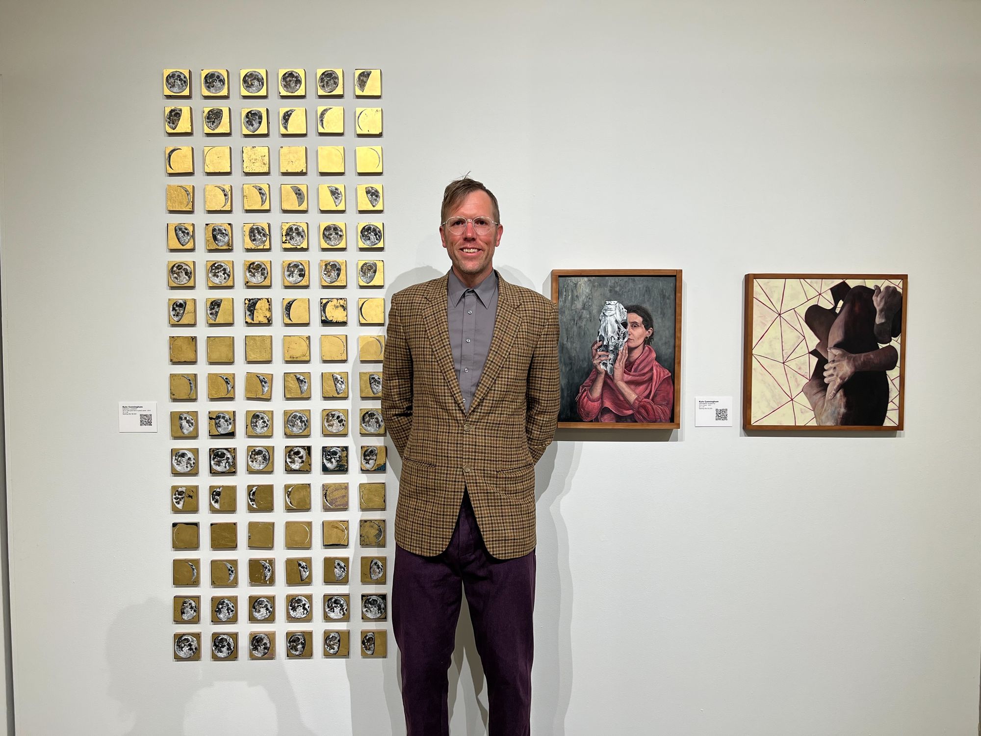 A man stands in front of a wall with paintings on it.