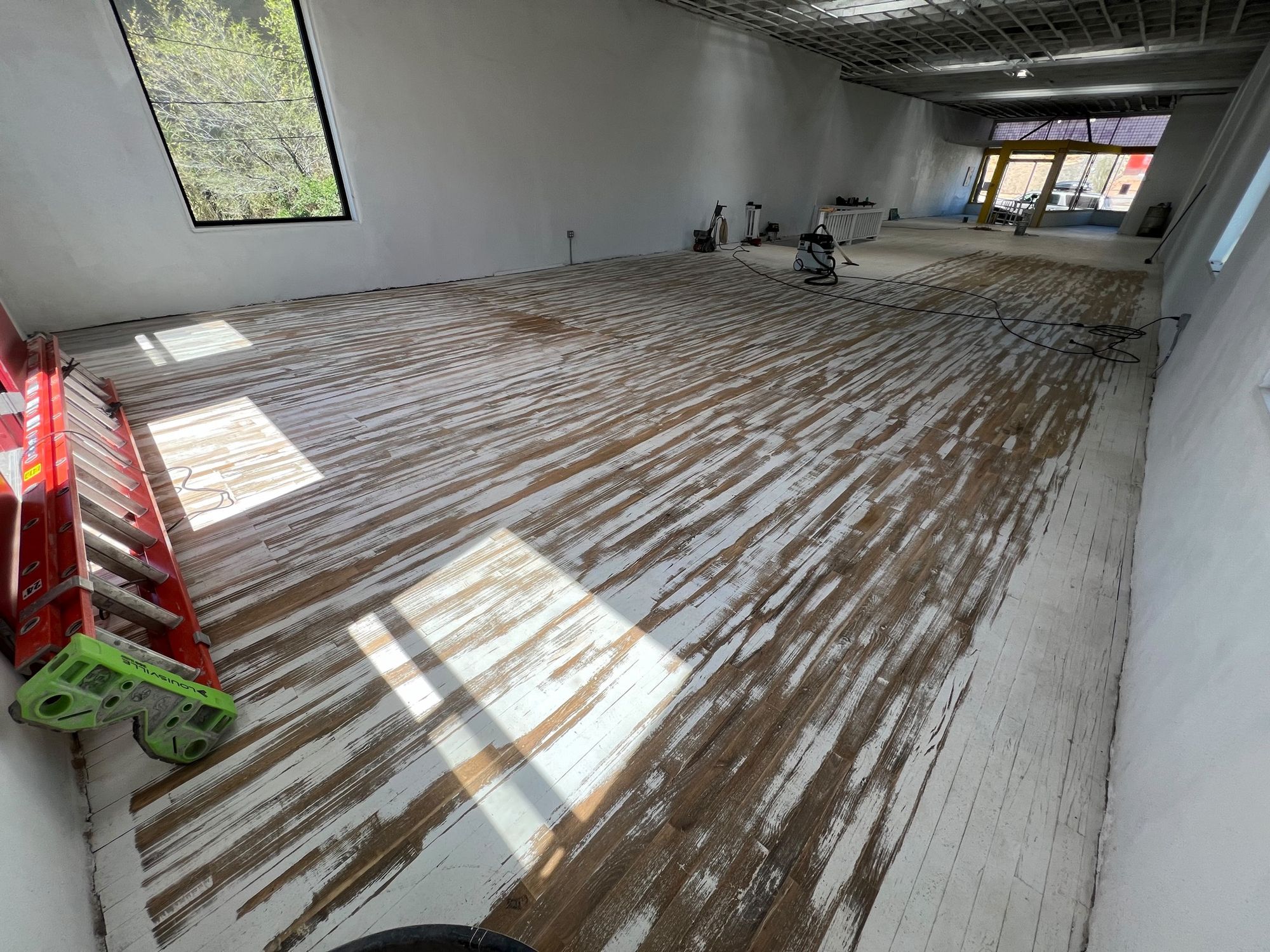 A wood floor with the first pass of sanding done, about 50 percent of the paint is gone.