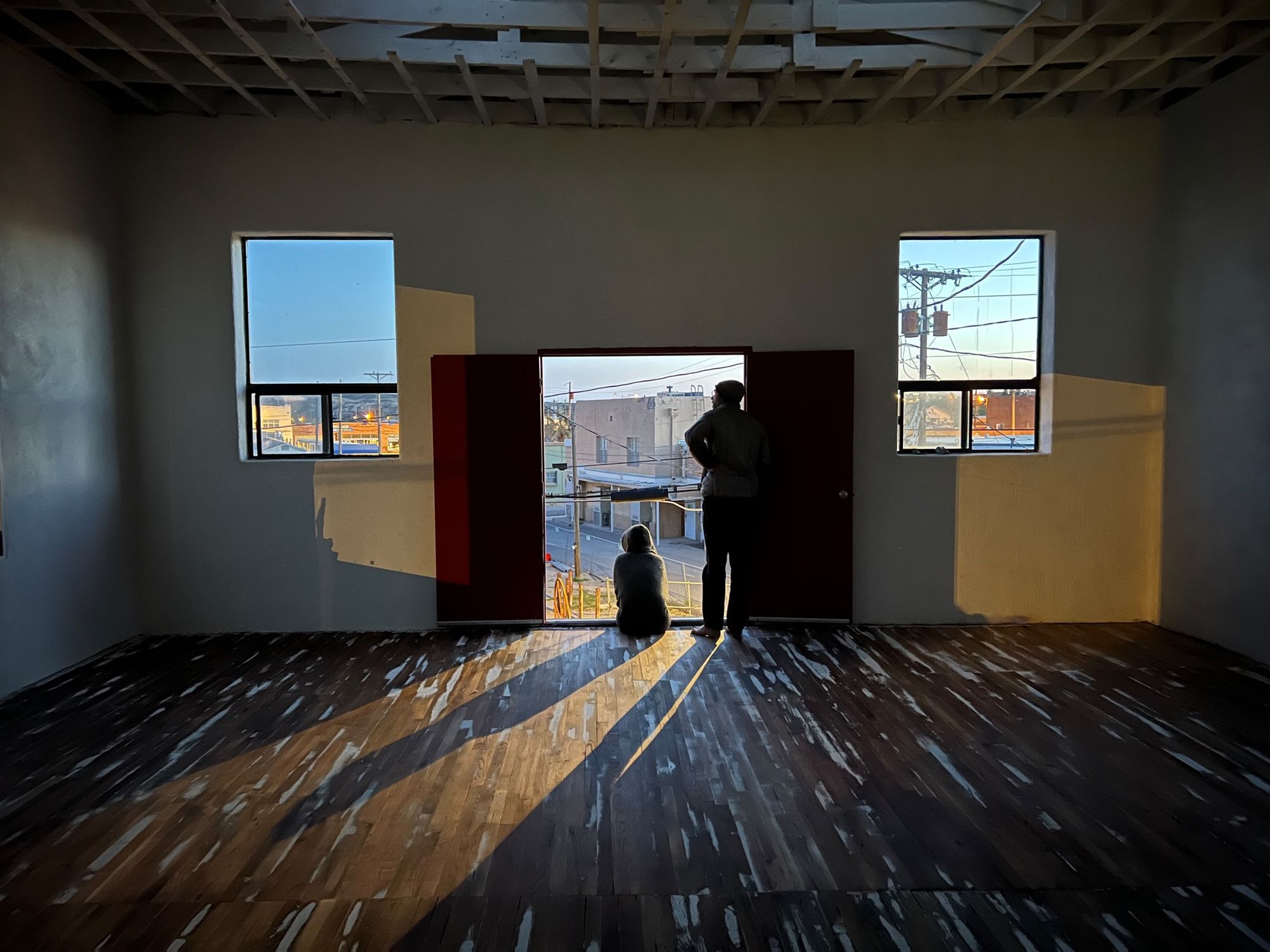 Two people one sitting and one standing in a door way at sunset overlooking a town.