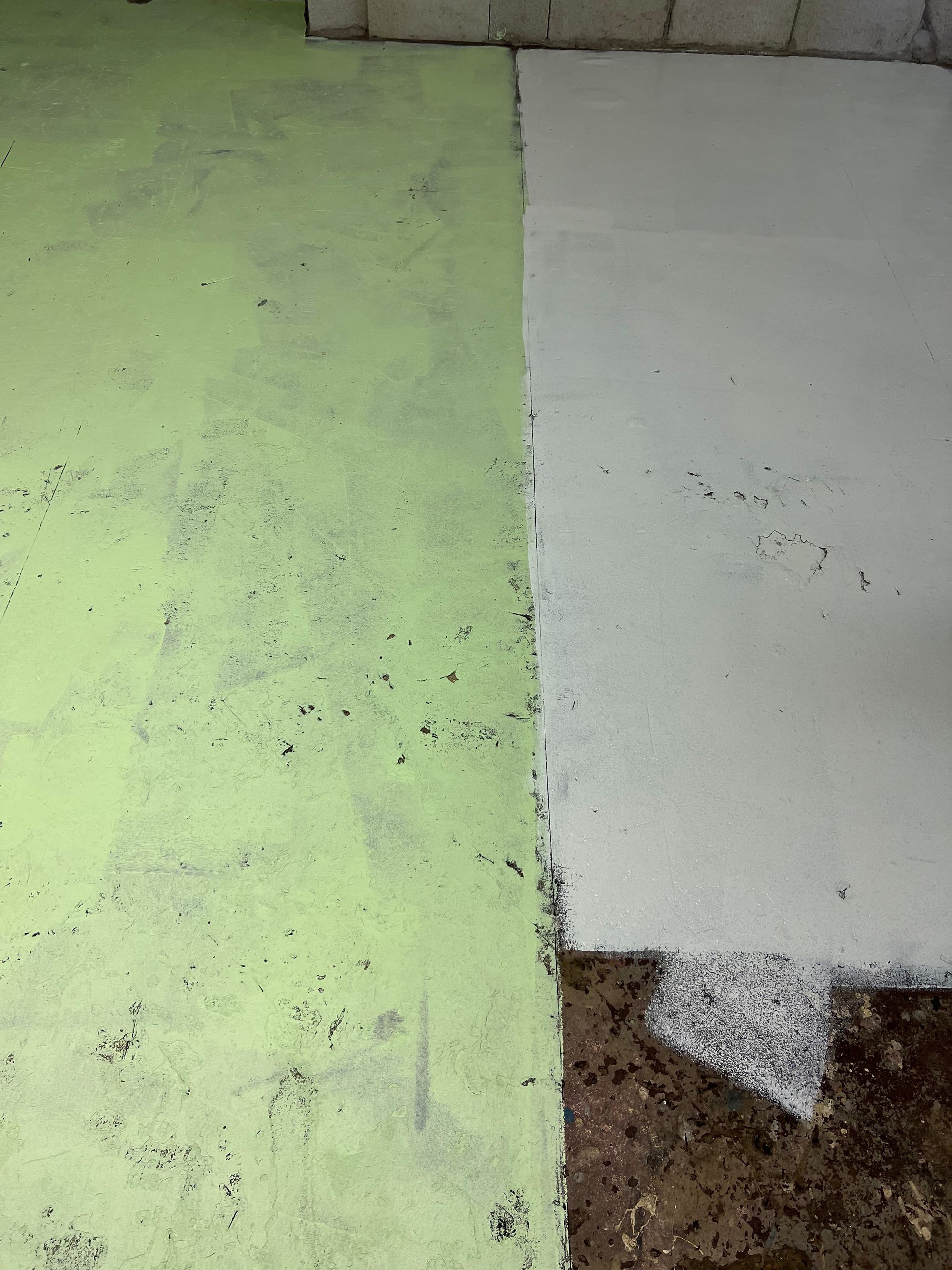 A floor primed with white paint on the right and painted green on the left. 