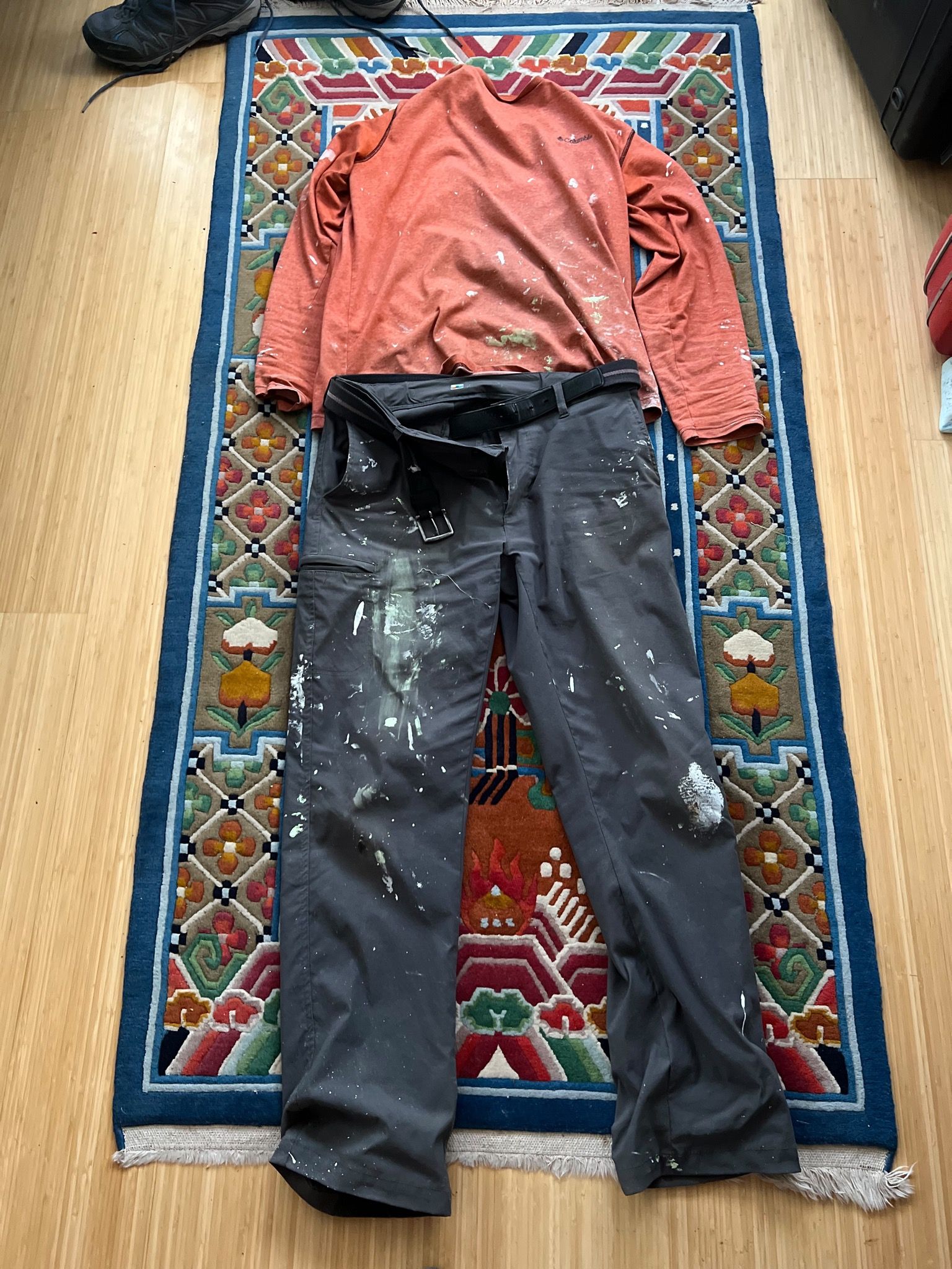 A pair of pants and shirt laid out on the floor. The clothes are dirty and covered in paint marks.