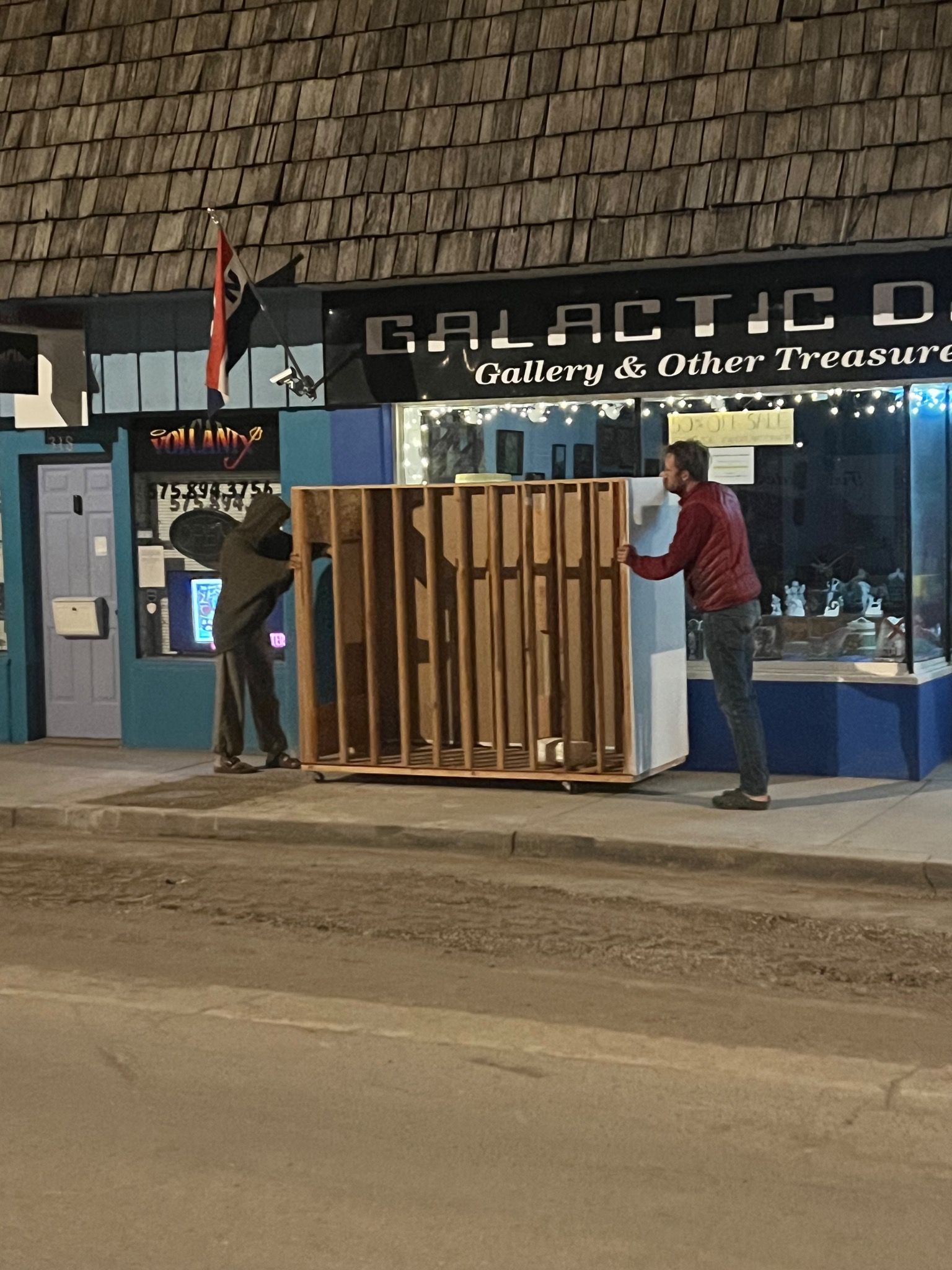 Two people push a painting rack down a sidewalk.