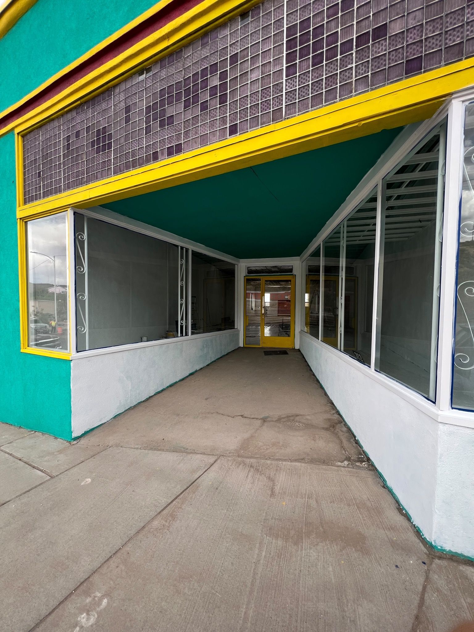 A long glass lined entry way to a building is freshly painted white over the existing teal.
