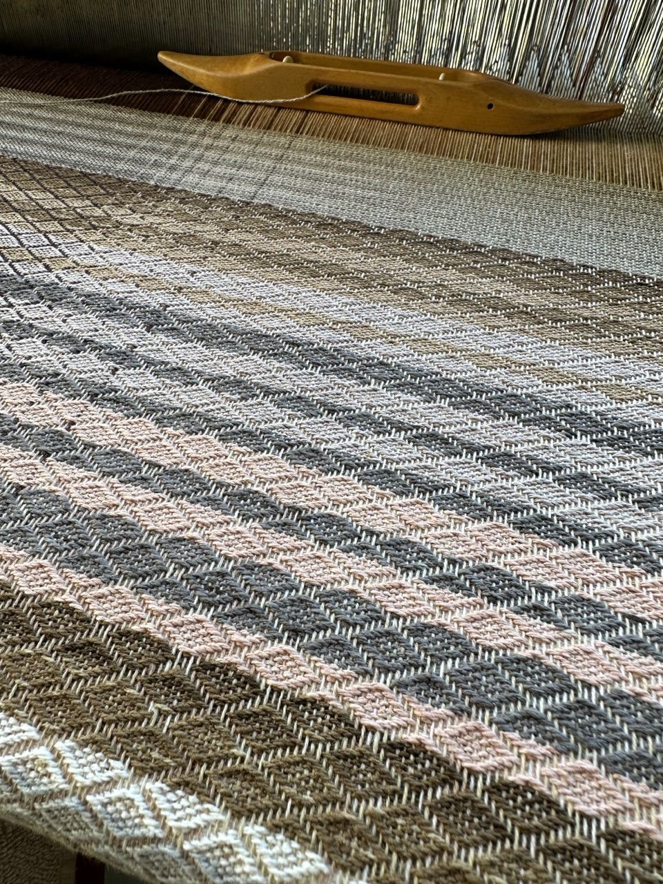 A detailed image of textured diamond pattern fabric on a loom, in soft naturally dyed shades of the rainbow.