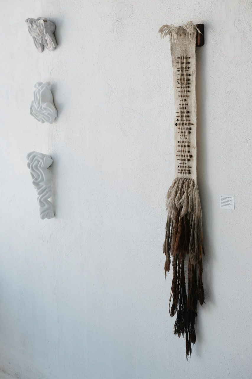 Handwoven wool, walnut wood and rusty nails wall hanging sculpture with long brown shaded fringe on a white wall