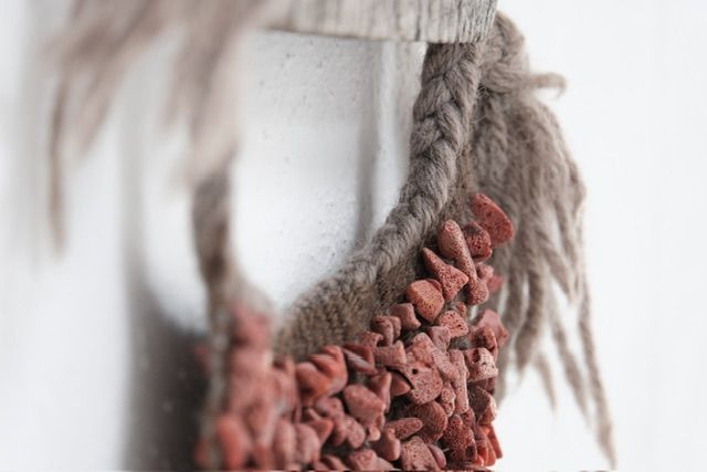 A detail of Red Coral & Wool Adornment hanging on a small oak frame on a white wall