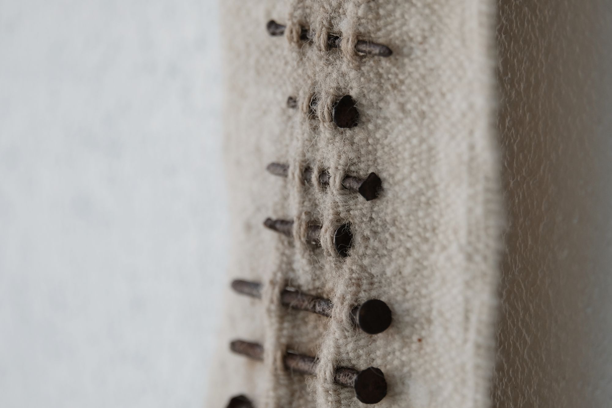 Handwoven wool, walnut wood and rusty nails wall hanging sculpture with long brown shaded fringe on a white wall