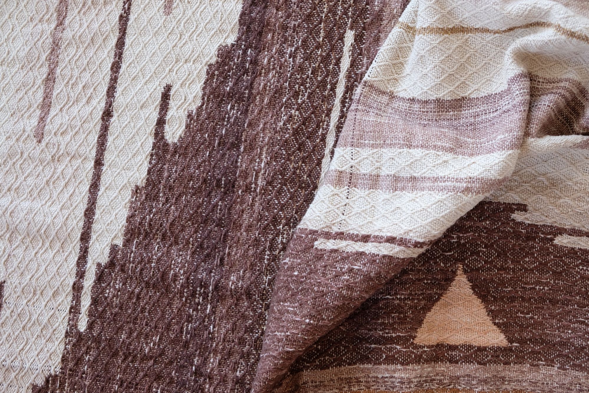 A large piece of handwoven fabric in shades of brown, cream and white rests on a dark wood floor