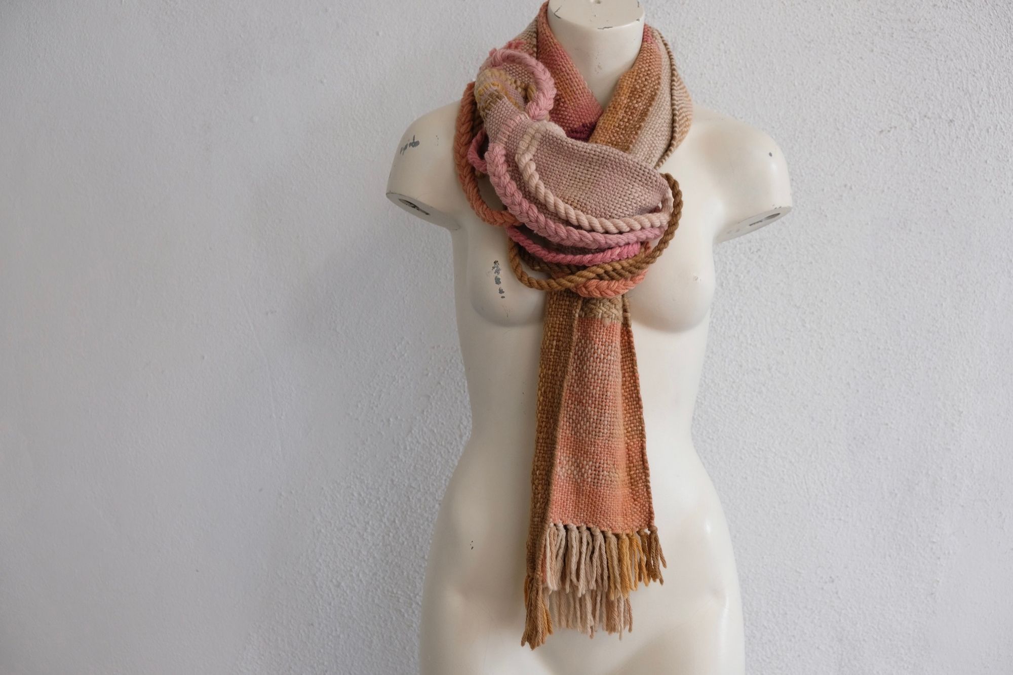 A softly colored chunky-sculptural scarf with thick braided and twisted rope-like details is displayed on a white painted mannequin