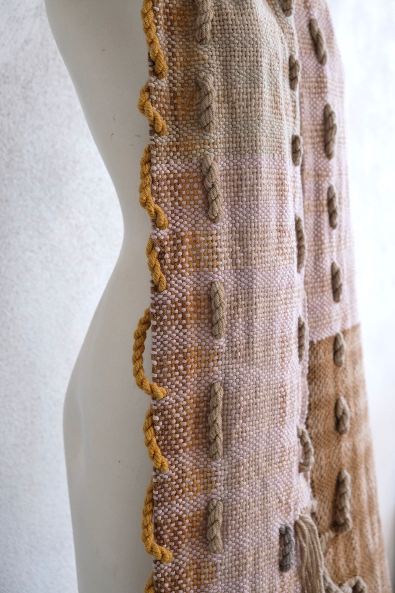 A softly colored chunky-sculptural scarf with thick braided and twisted rope-like details is displayed on a white painted mannequin