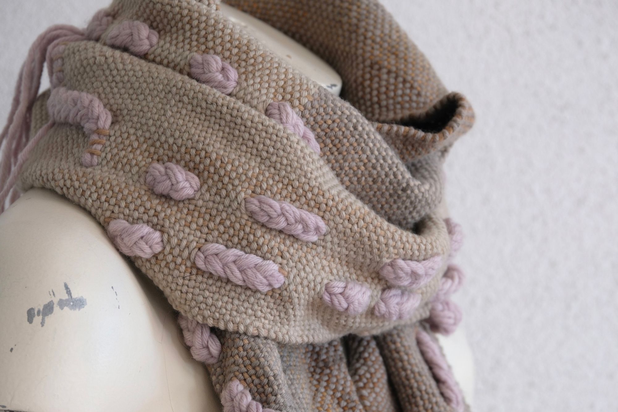 A softly colored chunky-sculptural scarf with thick braided and twisted rope-like details is displayed on a white painted mannequin