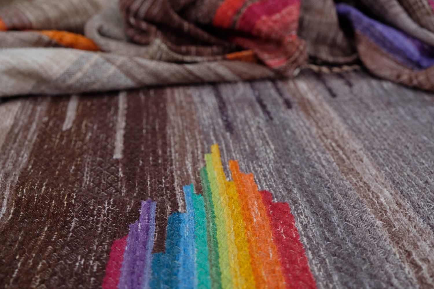 a detail of the centerpiece of a handwoven work. it is an abstract form of a rainbow, merging into rich shades of earthy brown and gray