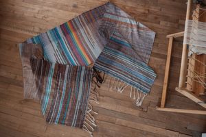 Handwoven fabric with a diamond weave pattern in shades of brown, blue and rainbow lays on a wooden floor