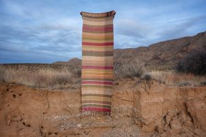 A detail of handwoven silk fabric in soft rainbow striped shades, naturally dyed, being held in a desert landscape