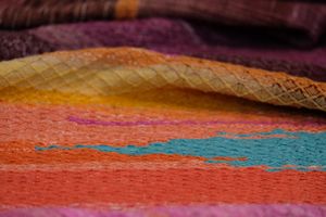 a close up view of handwoven, diamond pattern textured fabric in brilliant blues, orange and pink