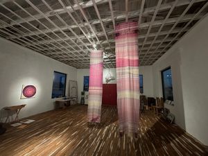 two handwoven fabrics in shades of pink hang in a large gallery space with wooden floors