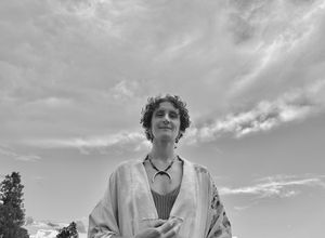 A black-and-white photo of a woman wearing a white kimono with a crescent moon necklace