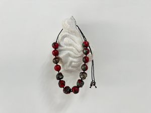 A necklace of cherry red and metallic silver clay beads hangs on a white marble sculpture