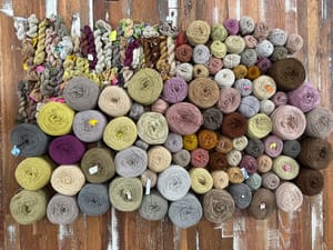 on a wooden floor lay 139 balls and skeins of naturally dyed merino wool, each a different shade 