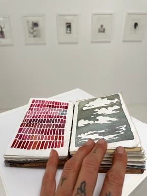 The hand of the artist holds open a small hand painted, hand bound book with wooden covers