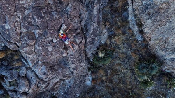 A birds eye view of a woman reclining on a rock outcropping wearing a rainbow handwoven cloak.