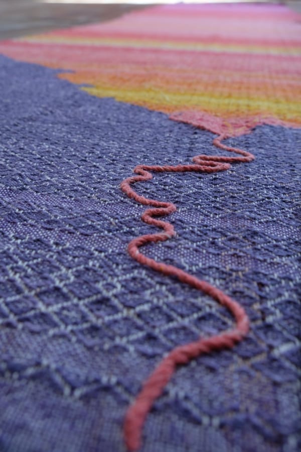 Details of a handwoven tapestry in deep purples and brilliant sunrise colors of pink, yellow and orange.